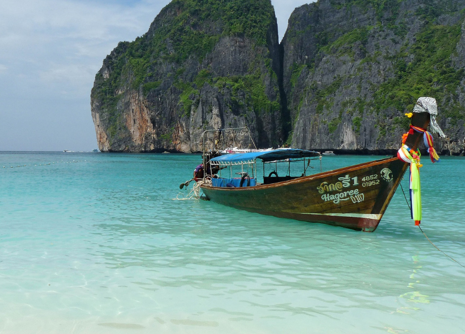 Tipica imbarcazione Thailandese che galleggia vicino a una spiaggia paradisiaca