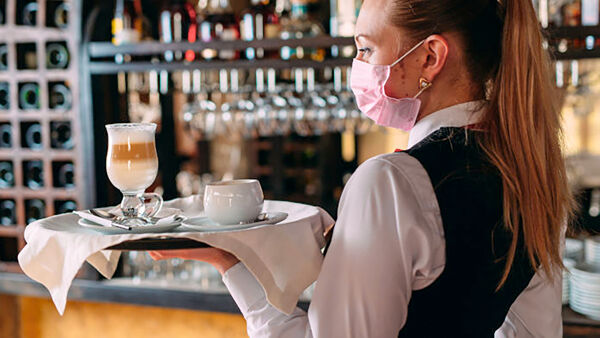 cameriera con mascherina rosa porta il caffè al tavolo in un bar
