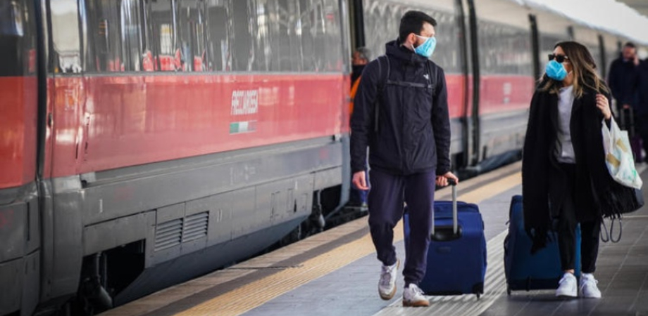 due giovani con la mascherina e le valigie si dirigono verso un treno per fare un viaggio in un'altraq regione