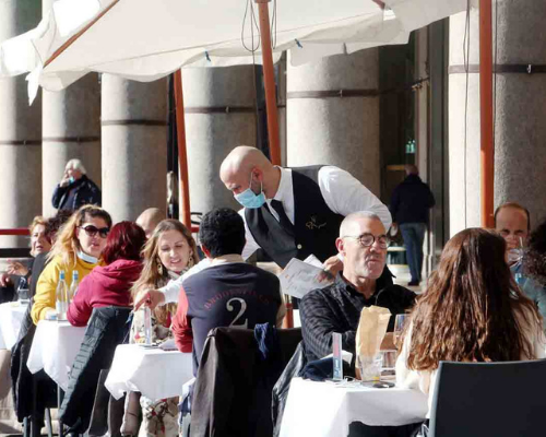 Un cameriere con la mascherina serve ai tavoli in un ristorante riaperto dopo il lungo periodo di chiusure da covid 19